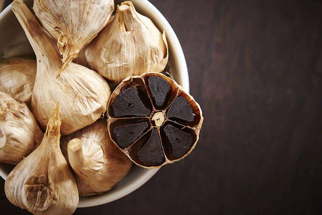 Bowl of garlic with a cut bulb showing the Benefits of Black Garlic.