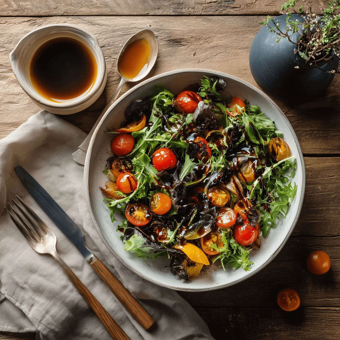 Salad dressed with Black Garlic Vinaigrette, featuring fresh greens and cherry tomatoes on a wooden table.