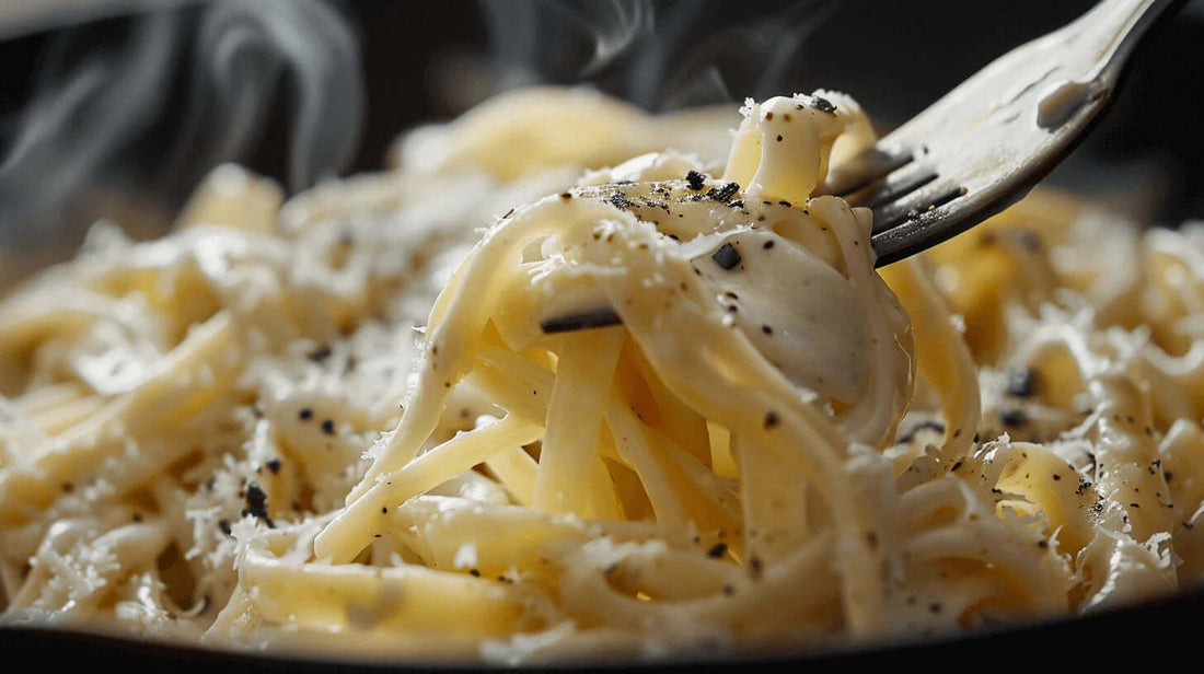 Black Garlic Pasta dish with creamy Alfredo sauce being twirled on a fork, topped with parmesan cheese and black pepper.